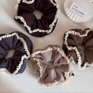 Close-up of four lace-trimmed ribbed knit scrunchies in earthy brown and grey tones