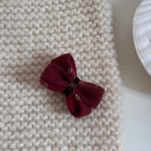 Vue rapprochée d'une pince à cheveux nœud en laine bordeaux sur un tricot blanc