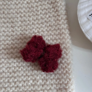 Gros plan d'un nœud papillon au crochet rouge foncé sur un fond tricoté de couleur crème