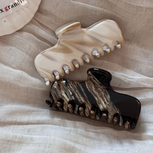 Detailed view of two French acetate hair claws with marble texture on linen fabric