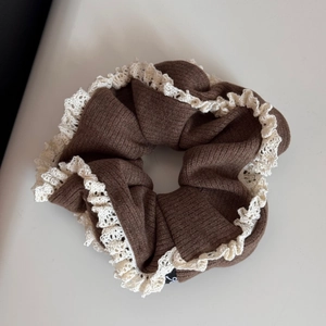 Detailed macro view of brown knit scrunchie featuring white double-layer lace edges