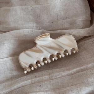 Detail of French acetate hair claw with cream and coffee marble texture on beige fabric