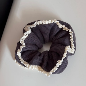Detailed close-up of dark grey knitted hair scrunchie with delicate ivory lace edges