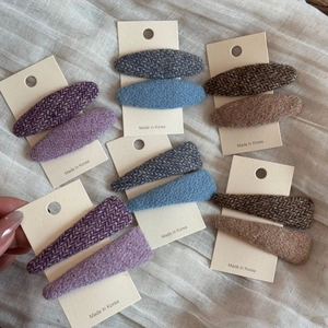 Dettaglio di fermagli in tweed viola, blu e marrone su supporto di cartoncino bianco