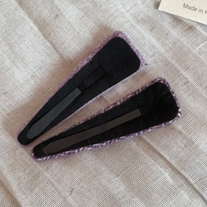 Dettaglio macro di due clip BB in tweed viola con fodera in feltro nero su tessuto