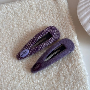 Detalle de dos pinzas para el cabello en tweed morado y tela sobre fondo textil blanco
