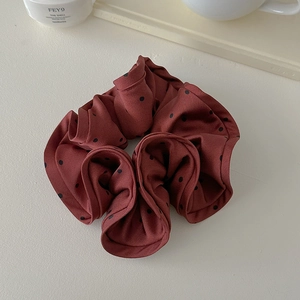 Close-up of a burgundy polka dot scrunchie on a minimalist beige background
