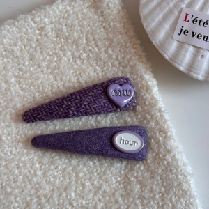 Vista macro de pinzas para el cabello en tweed púrpura con corazón de resina sobre blanco