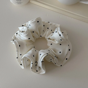Detailed macro view of white satin scrunchie with black polka dots and soft folds