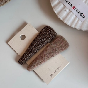 Dettaglio di fermagli per capelli BB in tweed marrone e viola su un cartoncino bianco