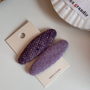 Dettaglio di due fermagli per capelli in lana viola su carta beige con trama a spina