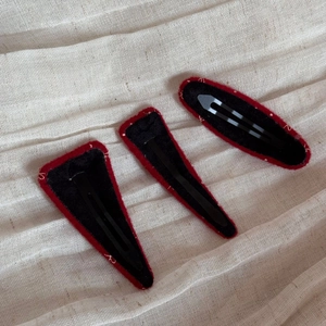 Dettaglio di tre fermagli per capelli BB in velluto rosso e tessuto nero su beige