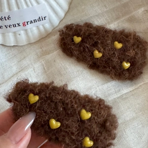 Braune Plüsch-Haarspangen mit goldenen Herz-Akzenten auf hellem Leinenhintergrund