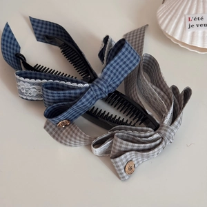 Détail de pinces banane élégantes avec nœuds à carreaux, dentelle et boucles dorées