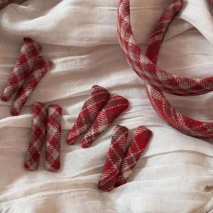 Detail of red plaid fabric hairbands and hair clips on a white linen textured background