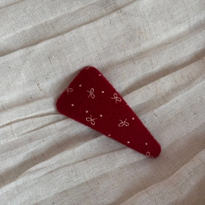 Dettaglio macro del fermaglio in feltro rosso scuro con ricami a fiocco e pois bianchi
