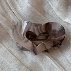 Detail of a large heart-shaped khaki marble acetate hair claw clip on linen fabric