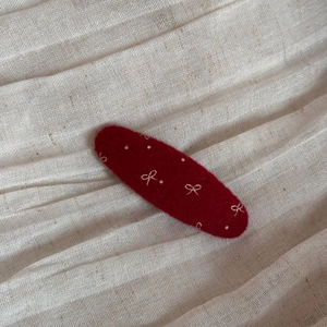 Dettaglio della clip per capelli in feltro rosso con ricamo a fiocco bianco e trama
