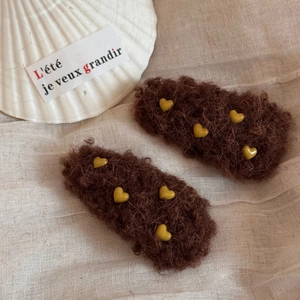 Detail von flauschigen braunen Haarklammern mit gelben Herzen auf beigem Stoffhintergrund