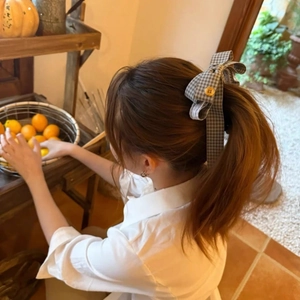 Détail de la pince à cheveux noeud en tissu écossais gris avec bouton jaune sur queue