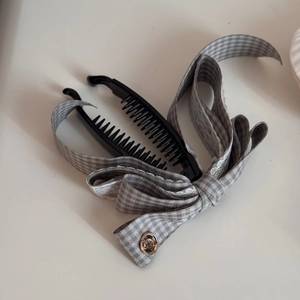 Détail d'une pince à cheveux banane avec nœud à carreaux gris et bordure en dentelle