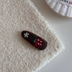 Close-up of vintage embroidered strawberry and floral patterns on a dark brown BB hair clip