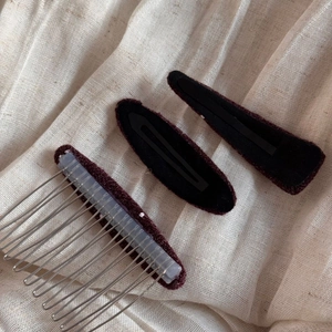 Close-up of elegant burgundy velvet hair clips and silver metal comb on beige fabric