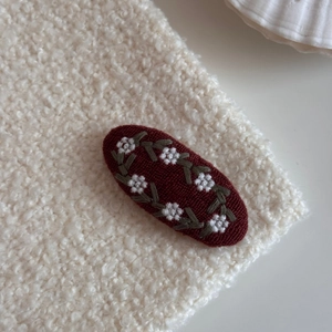 Macro shot of oval embroidery hair clip with white floral patterns on burgundy fabric