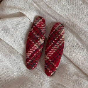 Close-up of a pair of red plaid wool BB hair clips on a beige linen fabric background