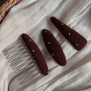 Detail of brown polka dot fabric hair clips and comb on a textured linen background