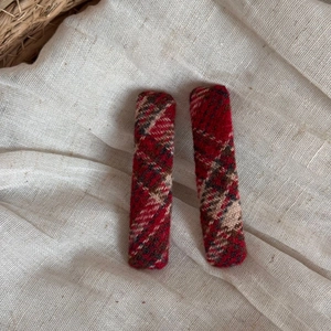 Detail showing two red plaid hair clips with Scottish tartan fabric on a textured background
