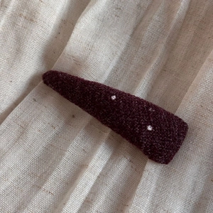 Close-up of a burgundy fabric hair clip with white polka dots on linen texture background