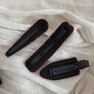 Macro shot of three burgundy velvet hair clips on beige linen including BB and duckbill styles