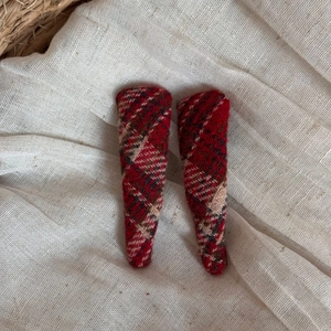 Close-up of red plaid wool hair clips on a beige linen fabric showing textured patterns
