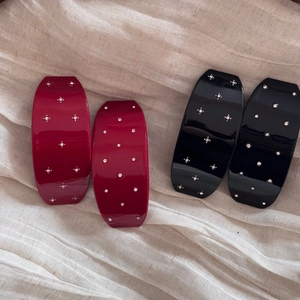 Détail de quatre barrettes à strass rouges et noires posées sur un tissu en lin beige