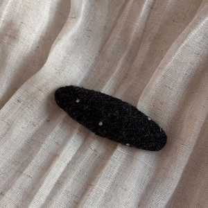 Detailed macro view of black felt polka dot hair clip on soft pleated fabric background