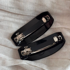 Détail de barrettes à cheveux noires brillantes avec boucles en métal argenté sur tissu