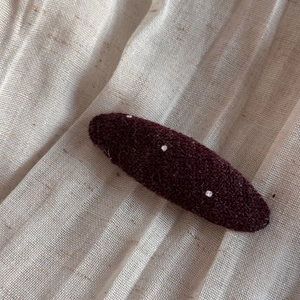 Close-up of a burgundy polka dot fabric oval hair clip on textured beige linen background