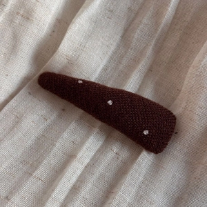 Close-up of a handmade dark brown knitted hair clip with white polka dots and soft texture