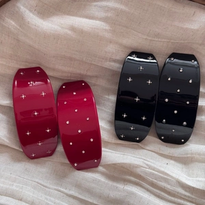 Détail de barrettes à cheveux rouges et noires avec strass sur tissu en lin naturel