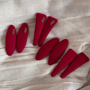 Close-up of handmade red felt hair clips set with golden metal tags on linen fabric