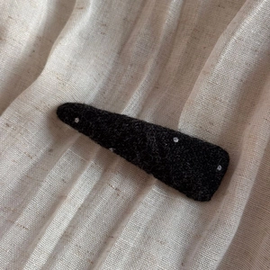 Close-up of black wool felt BB hair clip with white embroidered polka dots on linen fabric