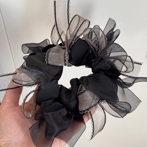 Detail of large black organza scrunchie with lace edges held in hand for size