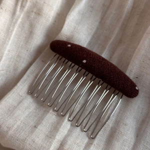 Close-up of a brown polka dot fabric hair comb with silver metal teeth on linen