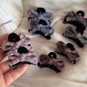 Close-up of wool tweed bow hair clips in purple, blue, brown and black on beige fabric
