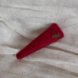 Detailed macro view of a red wool felt hair clip with a gold Handmade metallic logo