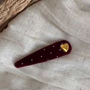 Macro detail of burgundy velvet hair clip with white polka dots and gold heart ornament