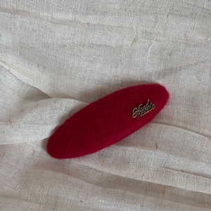 Detail of red wool felt hair clip with golden Handmade lettering on textured linen