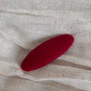 Macro shot of dark red wool felt hair clip on beige linen fabric texture detail