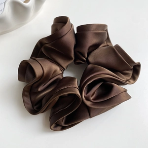 Détail d'un chouchou en satin marron foncé avec plis superposés et texture soyeuse